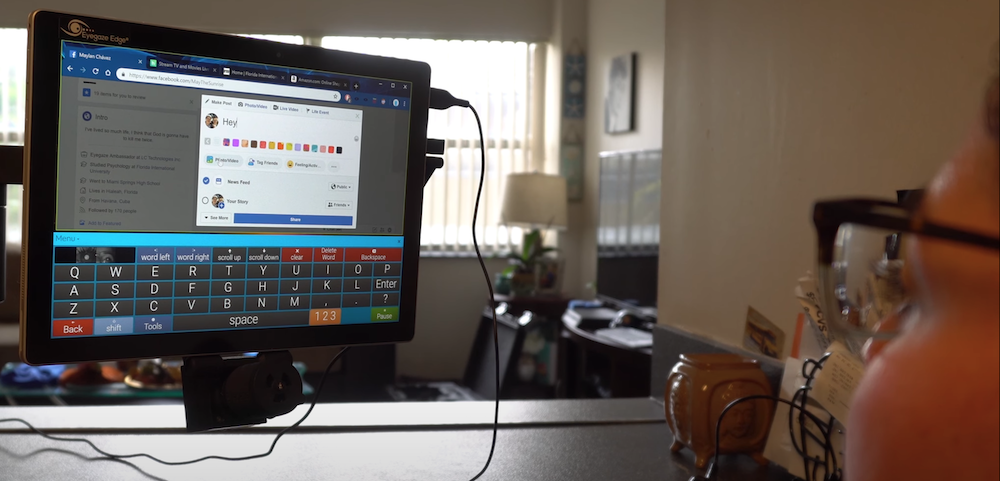 An eye-tracking user has a screen in front of them with Facebook loaded. They are using an on-screen keyboard to type a message.